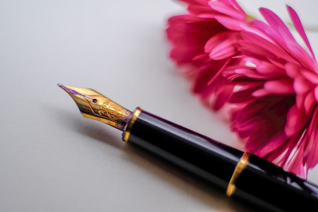 Black and gold-colored fountain pen beside pink flower